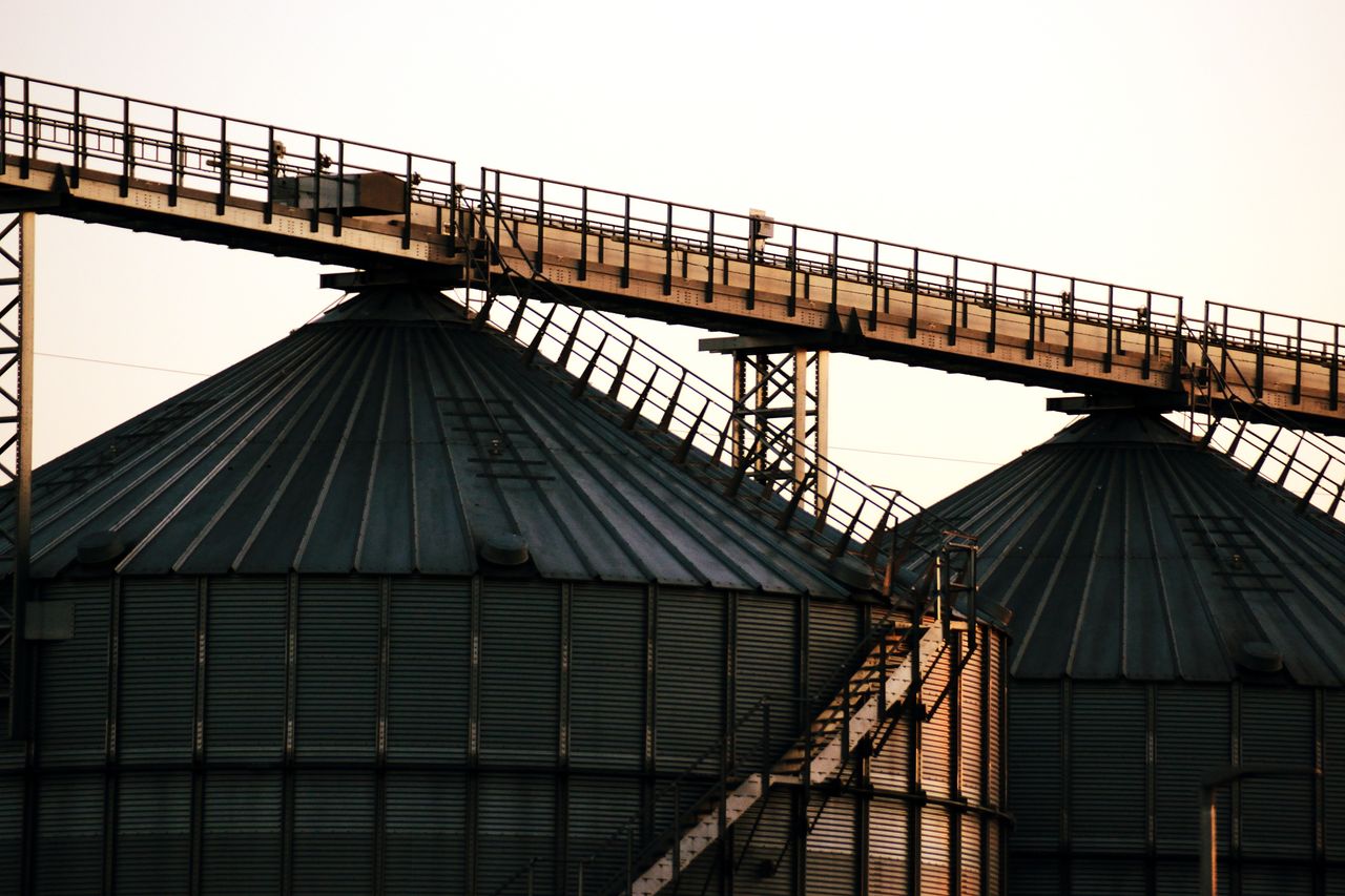 The Art of Drawing Readers In: Your attractive post title goes here Close-up image of industrial grain silos with overhead walkway at sunset, conveying modern industry.
